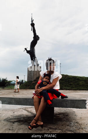 Managua, Nicaragua, Juni 1986; eine Frau und ihr Kind warten in einem Park im Zentrum von Managua neben einer fsln Regierung Statue zu Helden der Revolution. ' Stockfoto