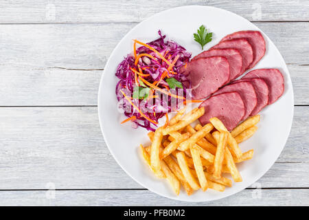 Scheiben geräucherter Kalbsfilet, Pommes frites und Rotkohl Salat mit Karotten, Fleisch, Tomaten und Petersilie auf Weiß rustikal Boards, Ansicht von oben Stockfoto