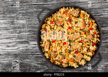Hausgemachte zubereitete Paella mit Fleisch, Pfeffer, Gemüse und Gewürze in eiserne Pfanne auf Holzbohlen, Kopie Raum links, Ansicht von oben Stockfoto
