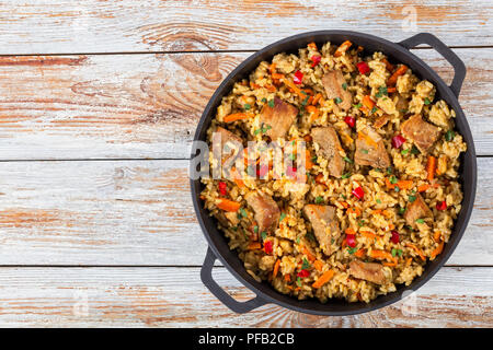 Hausgemachte zubereitete Paella mit Fleisch, Pfeffer, Gemüse und Gewürze in eiserne Pfanne auf weißem abblätternde Farbe holzbohlen, Ansicht von oben Stockfoto