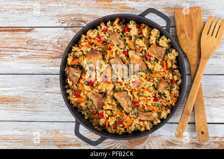 Hausgemachte zubereitete Paella mit Fleisch, Pfeffer, Gemüse und Gewürze in Eisen stewpan auf alten Dielen, Holzspachtel und Gabel auf Hintergrund, Nahaufnahme, Stockfoto