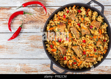 Hausgemachte zubereitete Paella mit Fleisch, Pfeffer, Gemüse und Gewürze in eiserne Pfanne auf weißem abblätternde Farbe holzbohlen, Chili auf Hintergrund, Aussicht f Stockfoto