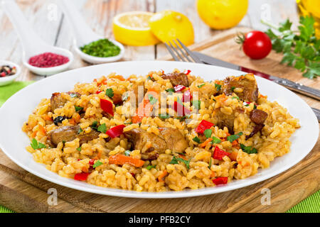 Paella mit Fleisch, Pfeffer, Gemüse und Gewürzen auf Teller auf ein Schneidbrett, Zitronenscheibe, Gewürze und Kirschtomaten auf Hintergrund, Ansicht von oben, Clos Stockfoto