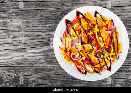 Mango, Brot panierte Hähnchenfleisch, Erdnüsse, Paprika, rote Zwiebel Salat auf einem weißen Teller mit Balsamico Dressing, auf alten Dielen, leeren Raum lef Stockfoto