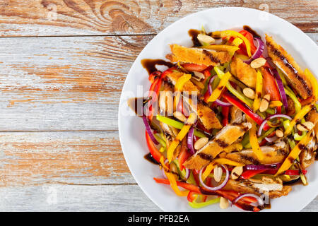 Mango, Brot panierte Hähnchenfleisch, Erdnüsse, Paprika, rote Zwiebel Salat auf einem weissen Teller, Balsamico Dressing, alte Bretter, Ansicht von oben Stockfoto