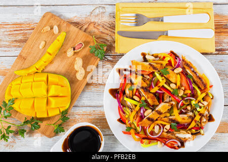 Mango, Brot panierte Hähnchenfleisch, Erdnüsse, Paprika, rote Zwiebel Salat auf einem weissen Teller, Balsamico Dressing, alte Bretter, Ansicht von oben Stockfoto