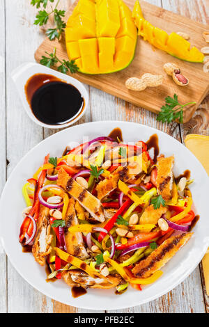 Mango, Brot panierte Hähnchenfleisch, Erdnüsse, Paprika, rote Zwiebel Salat auf einem weissen Teller, Balsamico Dressing, alte Bretter, selektiven Fokus Stockfoto