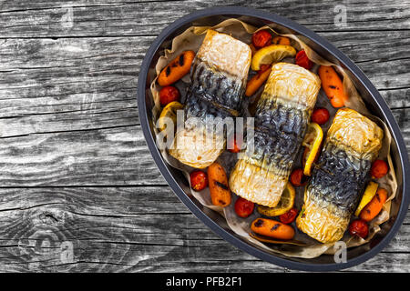 Brötchen - bis Filet Makrelen mit gegrillten Karotten, Kirschtomaten, Zitronensaft und Gewürzen in oval Auflaufform, auf dunklen Holzbohlen, Ansicht von oben Stockfoto