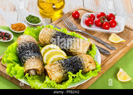 Gesunde gebackenes Filet Makrelen in Rollen auf Salatblättern und Zitronenscheiben auf weißem platter auf Schneidebrett mit Messer und Gabel, Ansicht von oben, c Stockfoto