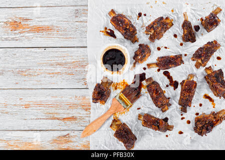 Leckere heiße klebrigen Ribs gewürzt mit pikanten Soja Knoblauch Ingwer Barbecue Sauce auf Pergamentpapier mit bürste an holz- abblätternde Farbe Hintergrund anzeigen Stockfoto