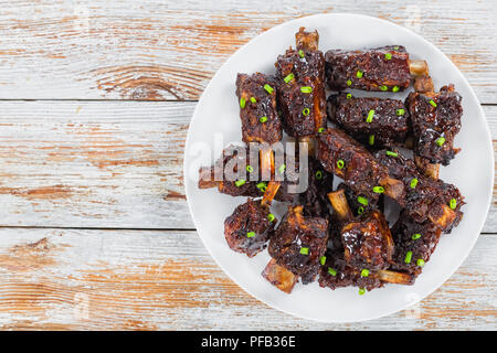 Chinesische würzige Spareribs auf weißem Teller, rote und grüne Chilischoten auf alten weißen Holz- Hintergrund, Ansicht von oben Stockfoto