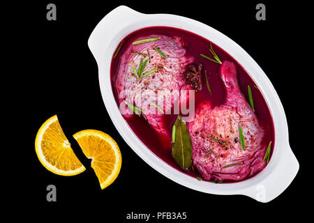 Raw Entenschenkel Vorbereitung für die Röstung in Rotwein mit Rosmarin und Gewürze in Auflaufform auf Schwarz, Vew von oben isoliert Marinierte Stockfoto