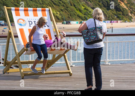 Bournemouth, Dorset, Großbritannien. 21 Aug, 2018. UK Wetter: warm und sonnig in Bournemouth Strände als sunseekers Kopf ans Meer, das Wetter zu genießen. Freunde haben Sie Spaß in der großen Liegestuhl für ein Foto auf Bournemouth Pier posieren. Credit: Carolyn Jenkins/Alamy leben Nachrichten Stockfoto