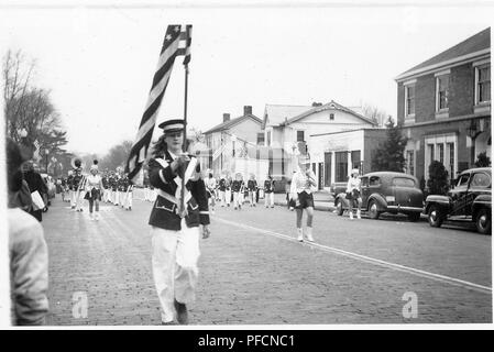 Schwarz-weiß Foto, zeigt eine Parade, von einem uniformierten jungen Holding eine amerikanische Flagge geführt, mit Majoretten und einer Blaskapelle im Hintergrund, Zuschauer und kahlen Bäumen auf der linken Seite, und mehrere Oldtimer vor der Gebäude auf der rechten Seite geparkt, wahrscheinlich in Ohio in den zehn Jahren fotografierte nach dem Zweiten Weltkrieg, 1945. () Stockfoto