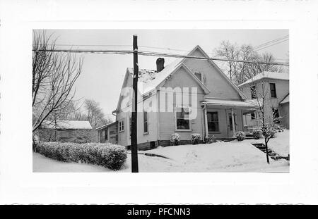 Schwarz-weiß Foto, mit einem kleinen, hellen Haus mit Gleisanschluss, eine überdachte Veranda, und Schnee auf dem Dach sichtbar, Vorgarten, Hecken, blattlosen Bäume und elektrische Beiträge, wahrscheinlich in Ohio in den zehn Jahren fotografierte nach dem Zweiten Weltkrieg, 1950. () Stockfoto