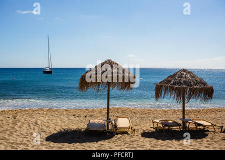 Liegestühle und Sonnenschirme aus Stroh am Strand in der Sonne. Stockfoto