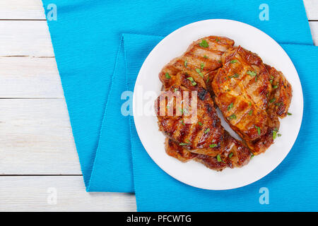 Perfekt gewürzt, saftig, lecker Gegrilltes Schweinekotelett mit Streifen auf weißem Teller serviert mit frischem Koriander, Ansicht von oben Stockfoto