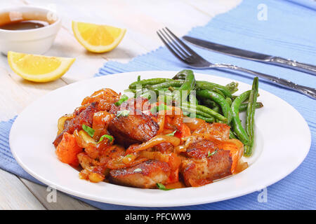 Klassische Fleisch Eintopf mit Zwiebel, Möhren und Gewürzen mit knusprig gebratenen grünen Bohnen auf weiße Platte, am Tisch Matte mit Gabel, Messer, Granatapfel Sauce und Lem Stockfoto