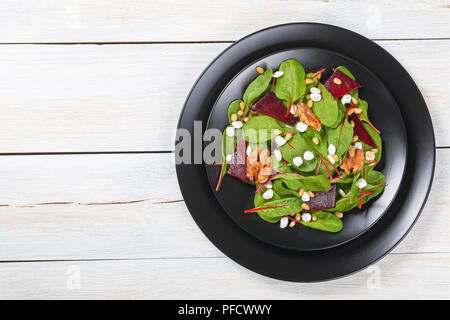 Frischen leckeren, gesunden Salat von Mangold Blätter, granulierte Hüttenkäse, gebackene Rote Beete Stücke und karamellisierten Walnüssen und Pinienkerne auf schwarzem Teller, Stockfoto