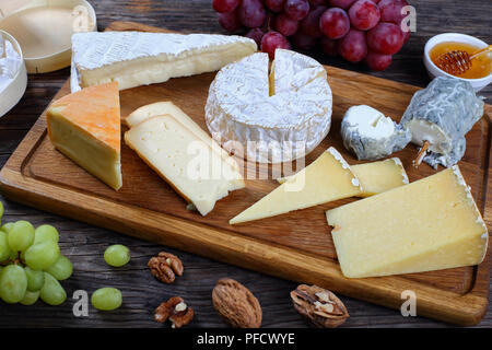 Der authentische französische Käse serviert mit Weintrauben, Honig und Nüssen auf Holzuntergrund mit Dreieck und runden hölzernen Behältern aus Pappelholz für Stockfoto