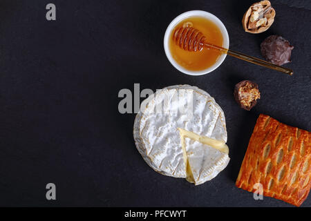 Weich, cremig, Oberfläche - gereifter Kuhmilch Käse Camembert schnitt in Slice auf schwarzem Schiefer Platte mit Honig, Nüssen, hausgemachte Schokolade Süßigkeiten und puff Pa Stockfoto