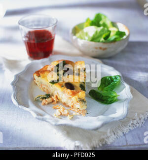 Scheibe Lachs und Blue Cheese quiche auf dem Teller neben Schüssel grünem Salat und einem Glas Saft im Hintergrund. Stockfoto