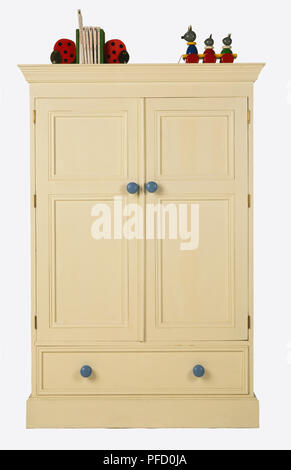 Creme double Kleiderschrank mit blauen Knöpfe und einzelnen Fach an der Unterseite, farbenfrohen Spielzeuge saß oben auf, Vorderansicht. Stockfoto