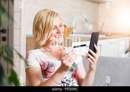 Hübsche blonde Frau auf dem Sofa sitzen und beim Einkaufen mit dem Smartphone, online kauf Konzept Stockfoto
