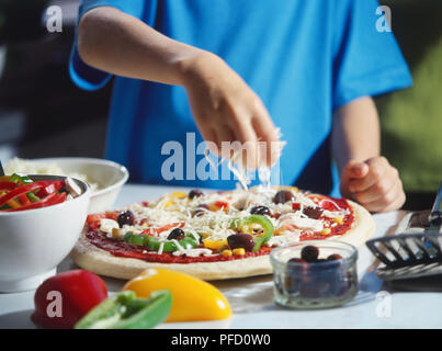 Käse bestreut, über Pizza mit pflanzlichen Aufstrichen, von Olivenbäumen umgeben und geschnittene Paprika in Schalen, Spachtel Stockfoto