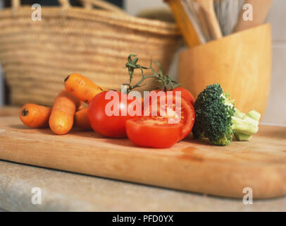 Nahaufnahme von Karotten, Tomaten und Brokkoli auf dickem Holz Schneidebrett, korbweide Warenkorb im Hintergrund Stockfoto
