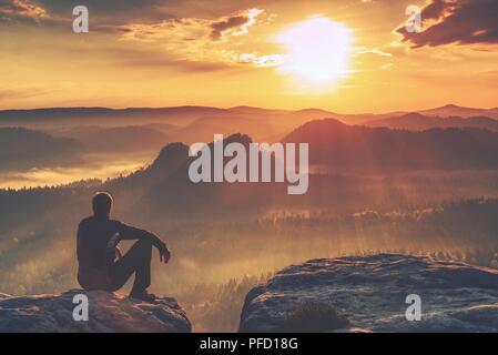 Müde tourist sitzt auf der Kante einer Klippe in die Ferne schauen. Wanderer ruht auf Mountain Trail. Unglaubliche Aussicht vom Gipfel. Stockfoto