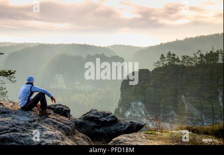 Müde tourist sitzt auf der Kante einer Klippe in die Ferne schauen. Wanderer ruht auf Mountain Trail. Unglaubliche Aussicht vom Gipfel. Stockfoto