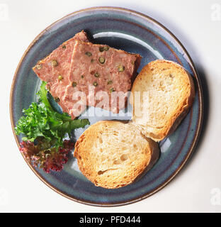 Zwei quadratische Scheiben von Port-bezogene Pastete gewürzt mit grünen Pfefferkörnern, auf blauen Platte mit zwei Scheiben knusprigem Brot und Salat serviert, Ansicht von oben. Stockfoto