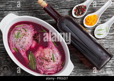 Raw Entenschenkel Vorbereitung auf marinierten Braten in Rotwein mit Gewürzen, Rosmarin und Orangenschale in der auflaufform auf alten Holzplanken mit Flasche r Stockfoto