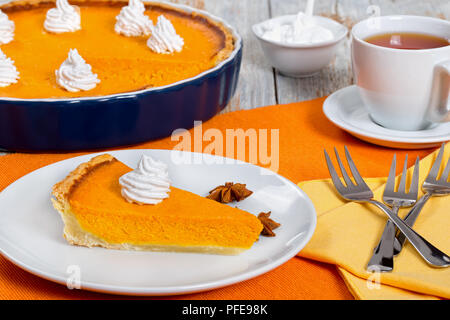 Scheibe der Kürbis tart-Dessert für Thanksgiving und Weihnachten, mit Schlagsahne. Tasse Tee und ganze Torte in Stücke geschnitten werden auf Hintergrund Stockfoto