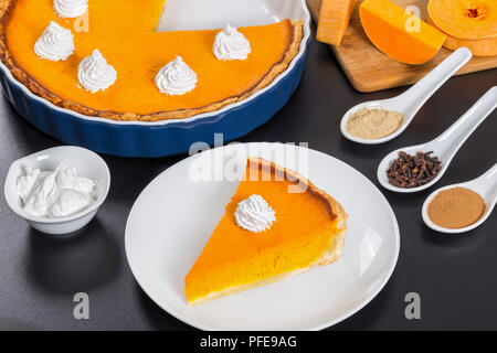 Scheibe der Kürbis tart-traditionellen Dessert für festliche Abendessen, mit Schlagsahne, Torte, Gewürze und Raw squash Schichten auf Schwarz backgroun Stockfoto