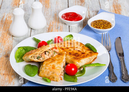 Gebratenes Fladenbrot Wraps mit Hähnchenfleisch auf weissem Teller mit frischem Spinat und Tomaten, Salz- und Pfefferstreuer, Ketchup, gefüllt und Französisch muss Stockfoto