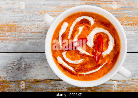 Würzig köstlichen asiatischen Kürbissuppe mit roter Thai Paste, Chili, Scheiben, und Sahne in weiße Suppe Tasse auf abblätternde Farbe Planken, Ansicht von oben, Clo Stockfoto