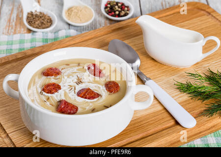 Lecker Bier und Creme würzige Suppe mit Kielbasa Wurst mit Kümmel bestreut in weiße Suppe Tasse auf Schneidebrett, Gewürze auf Hintergrund, authentische Stockfoto