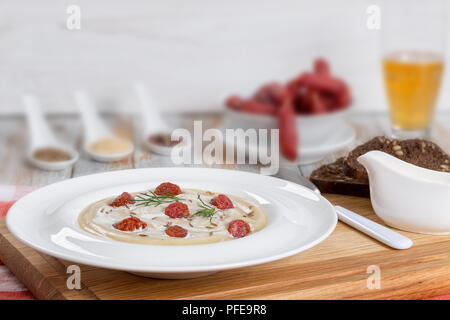 Lecker Bier und Creme würzige Suppe mit Kielbasa Wurst, Dill. und Käse in weiten rim Platte auf Schneidebrett, Gewürze und Bier Glas auf Hintergrund, Stockfoto