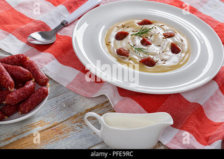 Lecker Bier und Creme würzig Winter Suppe mit Kielbasa Wurst, Dill. und Käse bestreut mit Kümmel in weiten rim Platte auf rot karierten Tabelle clo Stockfoto