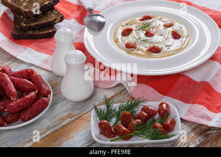 Lecker Bier und Creme würzig Winter Suppe mit gebratenen mini Salami Würstchen, Dill und Käse, mit Kümmel bestreut in weiten rim Platte auf rot kariert Stockfoto