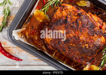 Ganze braten Schulter zog Schweinefleisch in Bräter mit reichen pikanten Marinade auf alten Holztisch mit Chili, Knoblauch und Rosmarin. Ansicht von oben, Stockfoto