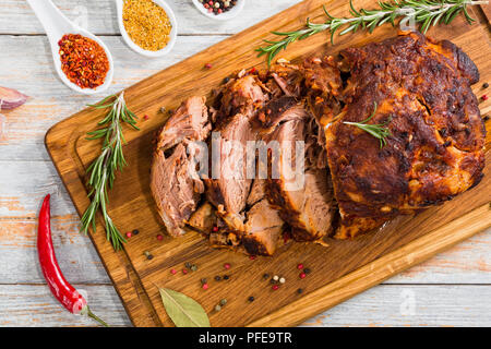 Gebratene Schweineschulter Schnitt auf Scheiben auf Schneidebrett auf weißem abblätternde Farbe Boards mit Knoblauch, Chili und Gewürze, Ansicht von oben Stockfoto