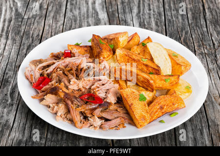 Teil zog langsam gekocht köstliche Fleisch Braten im Backofen mit gebratenen Kartoffelecken mit Petersilie auf weiße Platte auf dunklem Hintergrund sprengte, Stockfoto