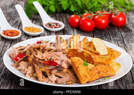 Teil zog langsam gekocht köstliche Fleisch Braten im Backofen mit gebratenen Kartoffelecken mit Petersilie auf weiße Platte mit Gewürzen, grünen sprengte und Stockfoto