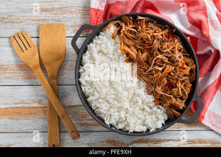 Langsam zog gekochte Schweineschulter vom Grill im Backofen mit langkörniger Basmati Reis in Eisen stewpot mit Küchentuch, auf Holz- Tabelle, Ansicht von oben Stockfoto