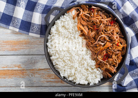 Langsam zog gekochte Schweineschulter vom Grill im Backofen mit langkörniger Basmati Reis in Eisen stewpot mit Küchentuch, auf Holz- Tabelle, Ansicht von oben Stockfoto