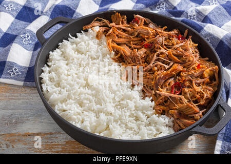 Langsam zog gekochte Schweineschulter vom Grill im Backofen mit langkörniger Basmati Reis in Eisen stewpot mit Küchentuch, auf Holztisch, Ansicht von oben, Cl Stockfoto