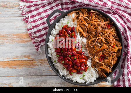 Langsam zog - gekocht köstliche würzige Fleisch mit Reis und herzhaften gebackene Bohnen bestreut mit Frühlingszwiebeln in stewpot mit Küchentuch, auf Holztisch, vi Stockfoto